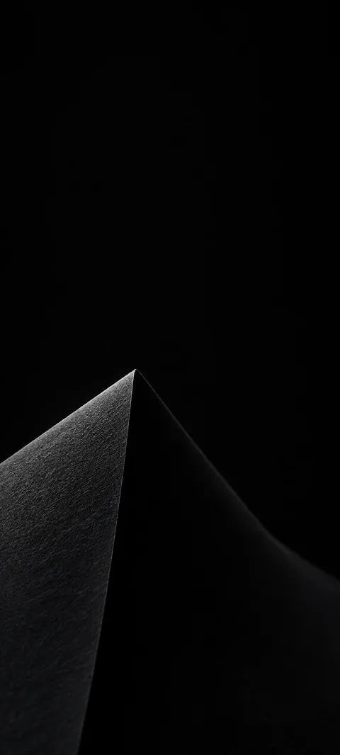 Charcoal paper-like fold with one dim gray textured face and a sharp point against black.