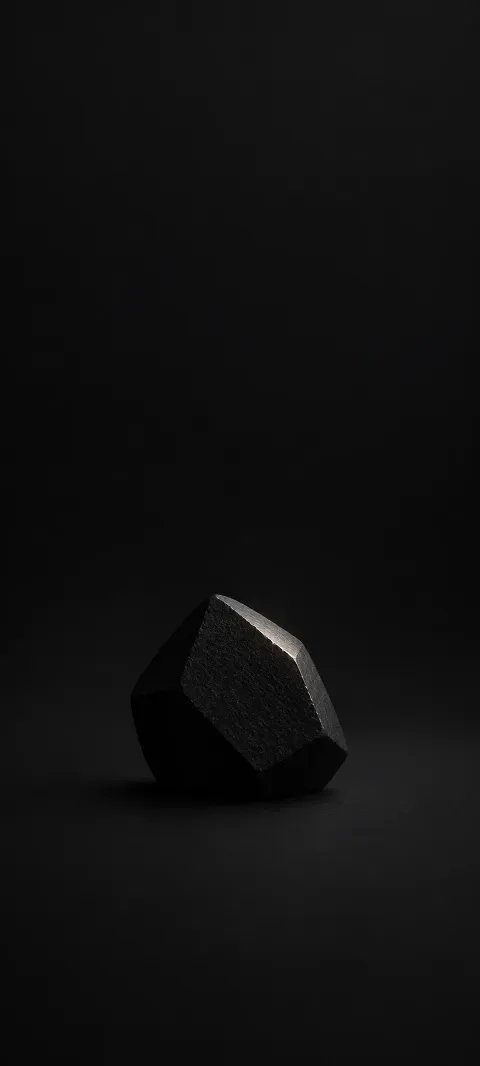 A faceted black stone rests on a nearly black surface.