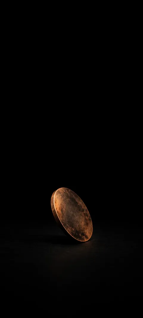 Small tilted tarnished copper disc with a warm lit edge on a black background.