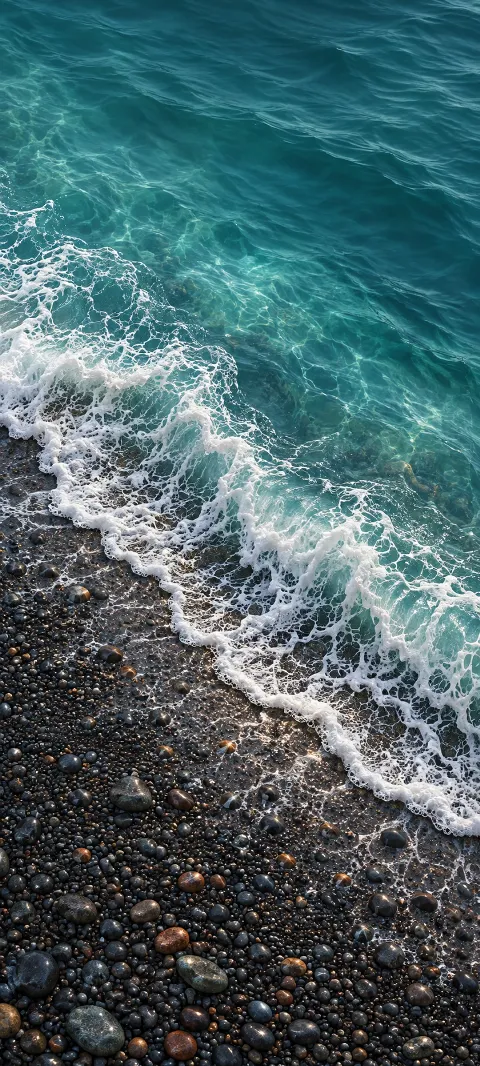 A diagonal white seafoam edge over dark pebbles beside clear teal water.