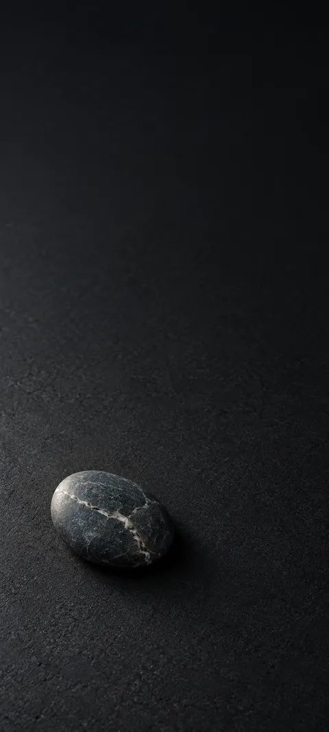 Dark oval pebble with a white quartz vein on a nearly black surface.