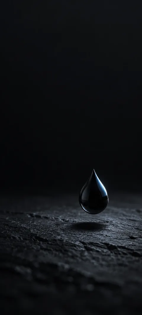 Black teardrop floating above dark textured slate with a small blue reflection.