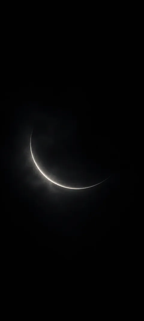 A thin ivory crescent glows within faint graphite haze on a black background.