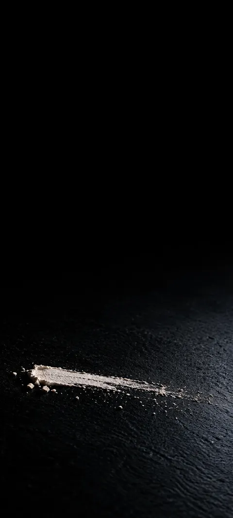 Short ivory chalk stroke and loose grains on a black textured surface.