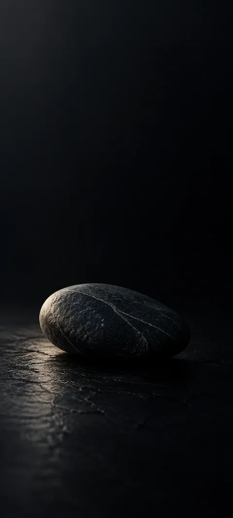 A charcoal stone with a pale diagonal vein on a dark surface.