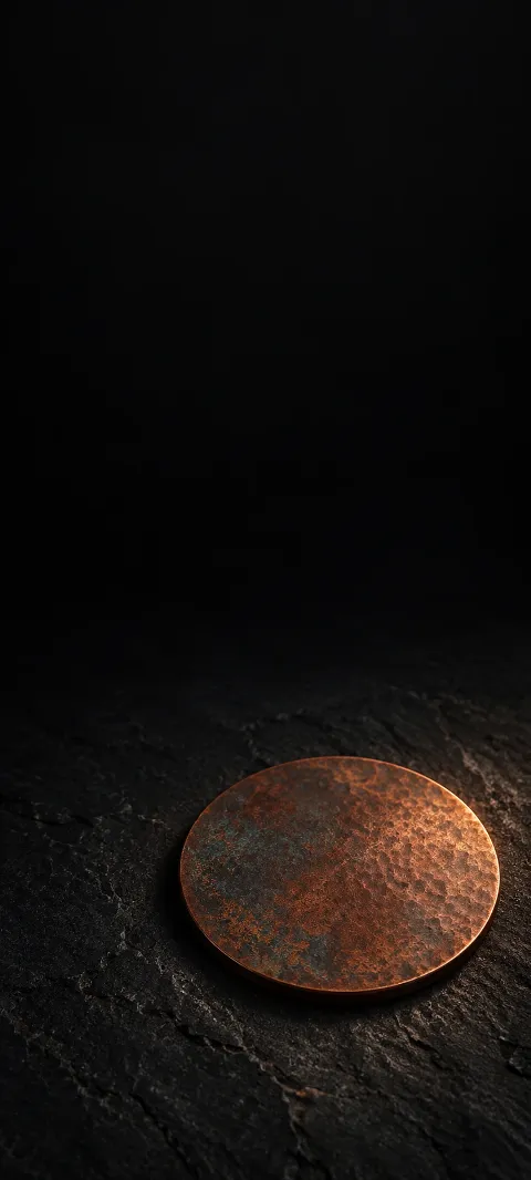 Flat patinated copper disc on a rough black stone surface.