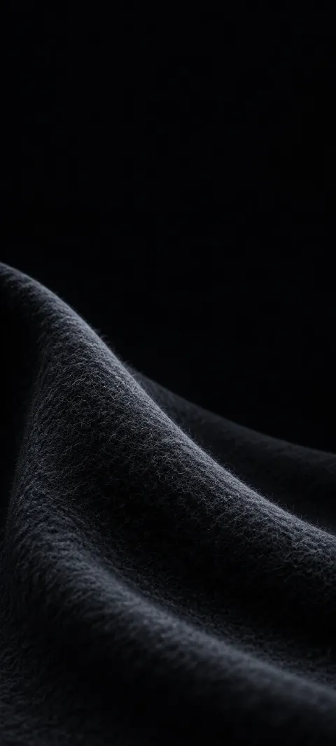 Close view of a charcoal felt fold with fine fibers and a soft cool rim.
