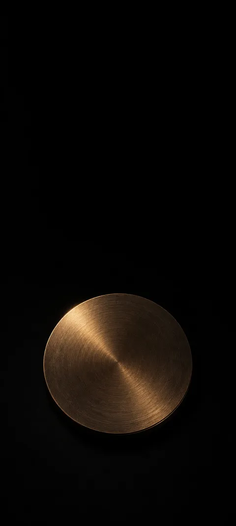 A round brushed bronze disc with a dim golden reflection against black.