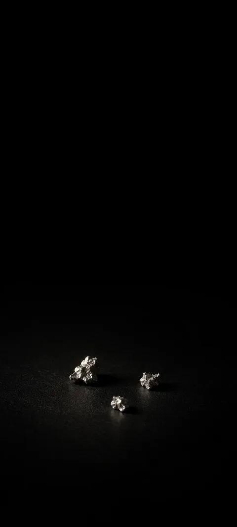 Three small irregular silver grains arranged in a triangle on a black surface.