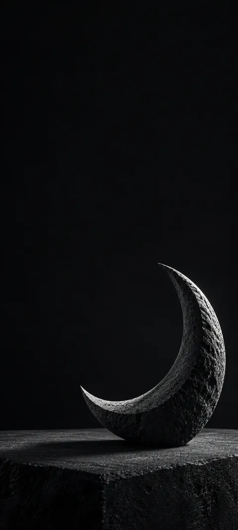 Dark graphite crescent sculpture on a stone slab with silver edge light.