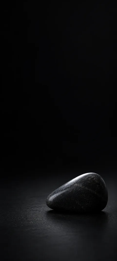 A rounded black wedge stone with a cool ridge highlight on a dark surface.
