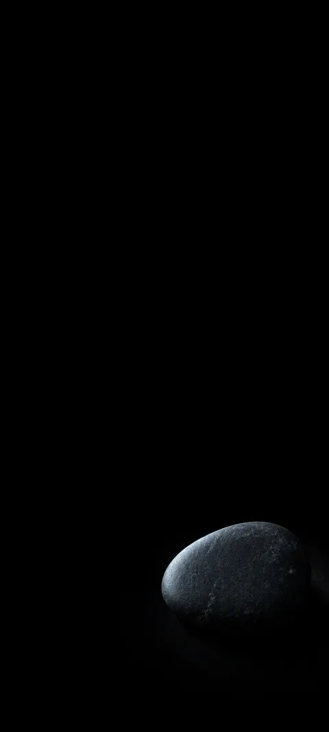 Single gray slate pebble with a cool lit edge near the bottom right of a black field.