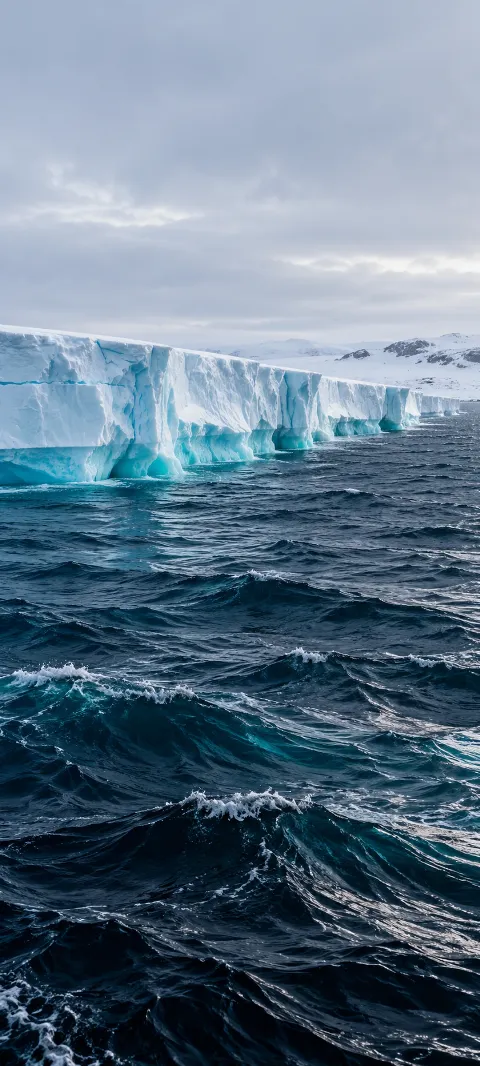 Dark blue ocean waves beside a white ice shelf with turquoise crevices.