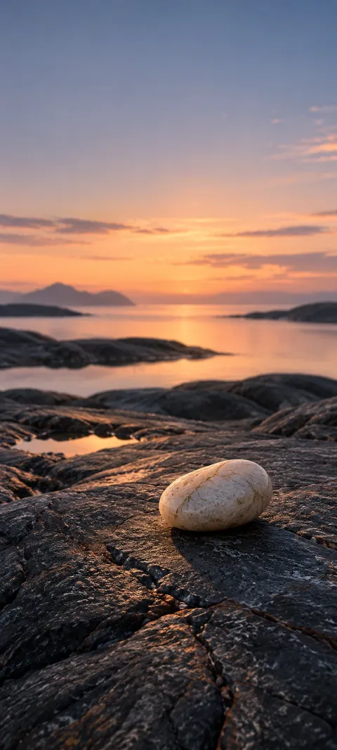 A pale pebble rests on dark wet stone beside sunset water.