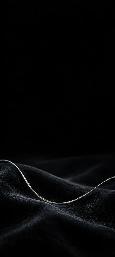 Fine pale silk thread curving over dark velvet against black.