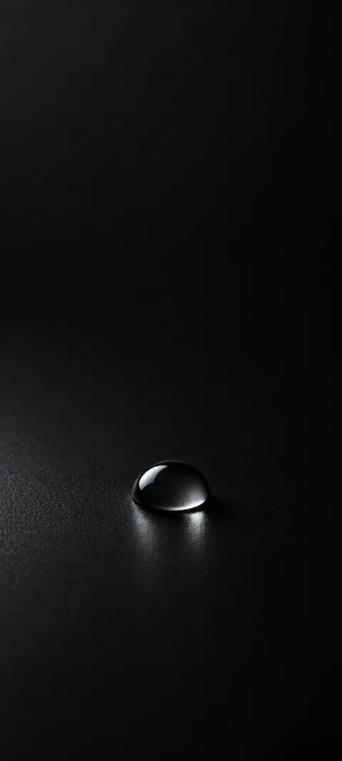 Small glossy black droplet on a dark textured studio surface.
