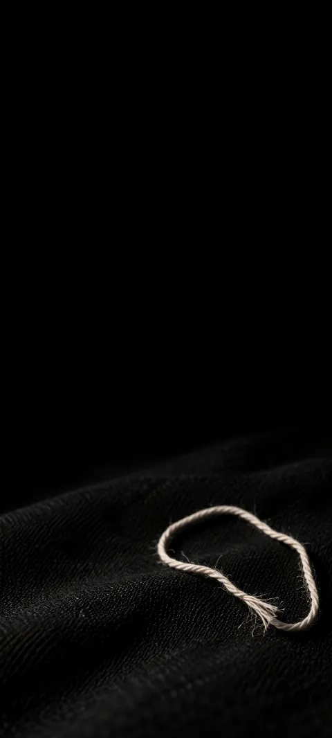 A loose ivory thread loop with a frayed end on black woven cloth.