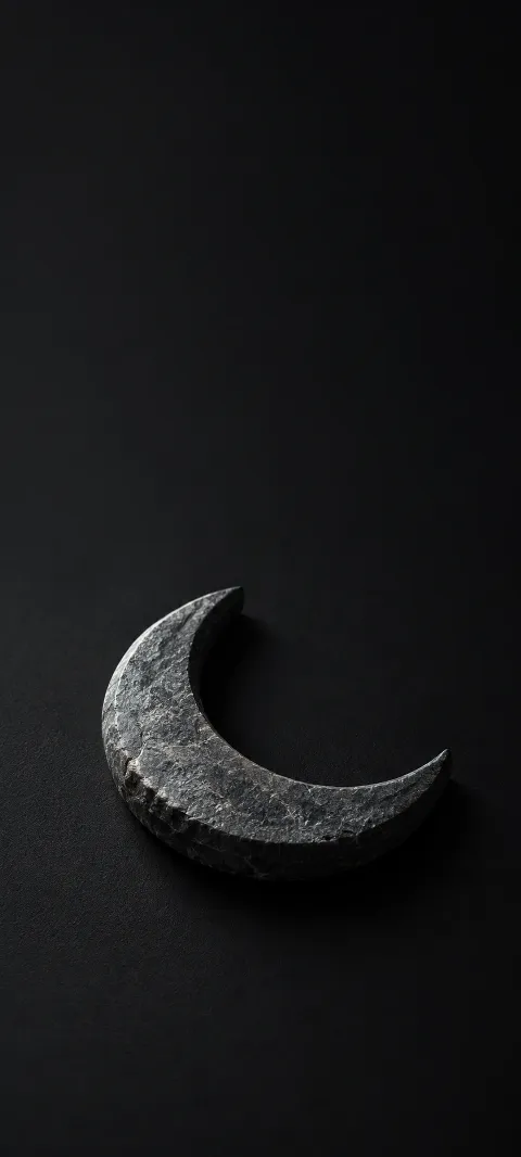 A small thick graphite crescent stone lying on matte black with cool edge light and a short shadow.