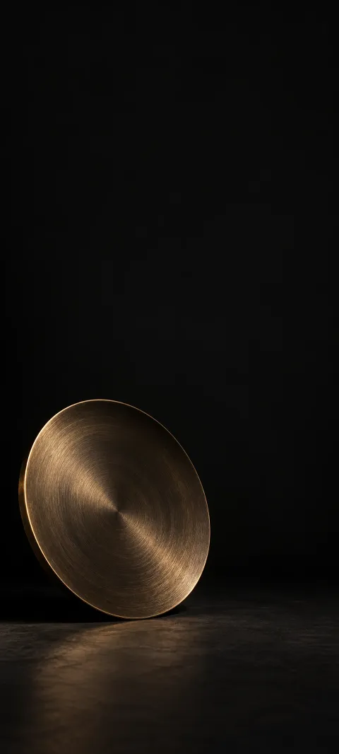 Single brushed bronze plate leaning on a dark studio floor.