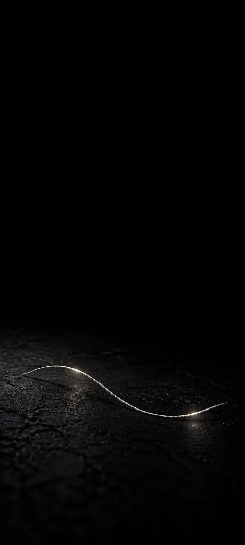 A single curved silver thread lying on textured black with small soft glints.