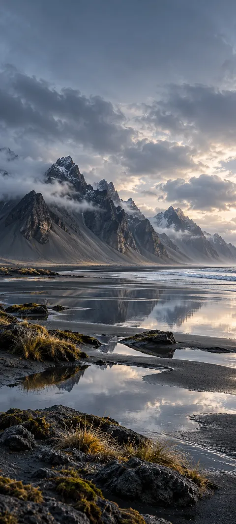 Dark basalt mountains meet a reflective gray shore.