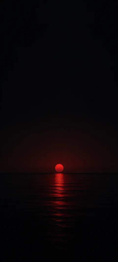 Small red disc at a low horizon with a red reflection on dark rippling water.
